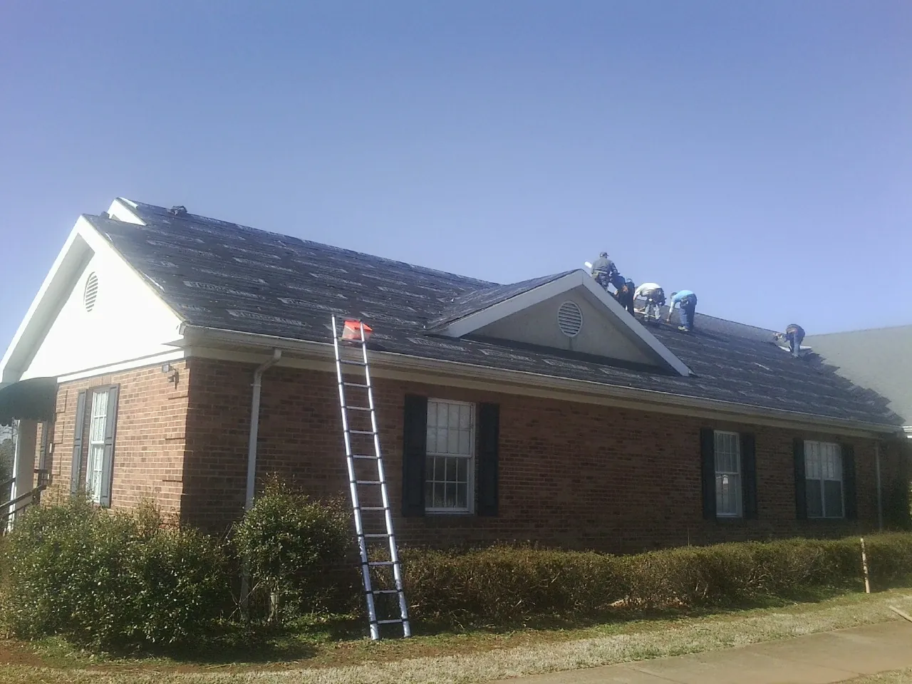 Crew tearing shingles off a brick ranch roof with a ladder set — Emergency Roof Repair work by our crew in Kilmarnock
