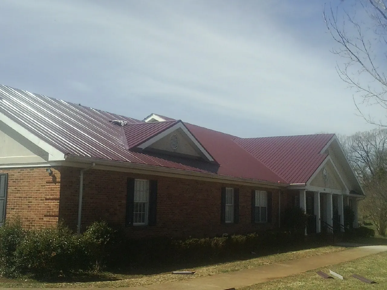 Red metal roof with gabled entries on a long brick building, from a Hail Damage Roof Repair job in Kilmarnock