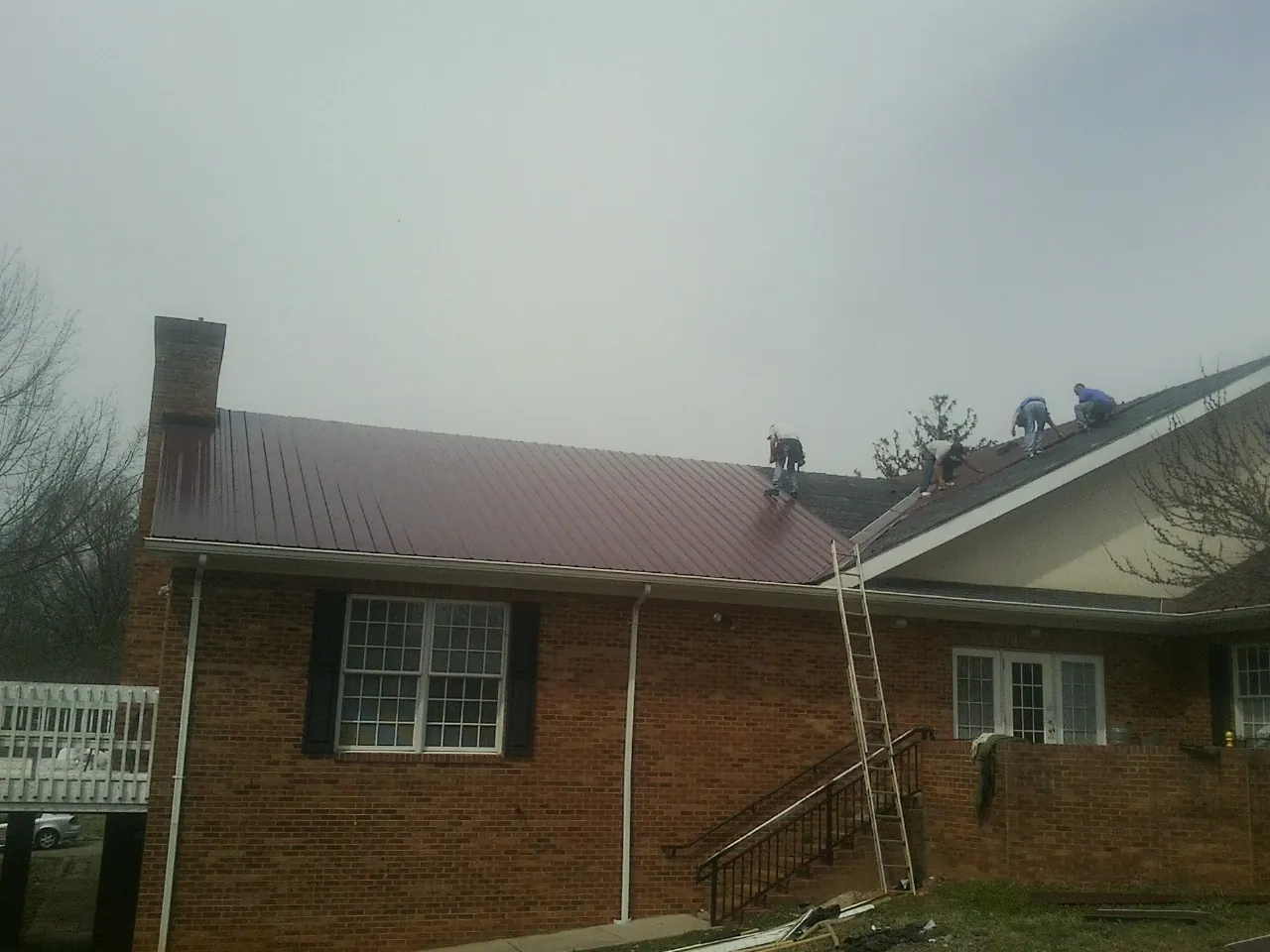 Crew setting red metal roofing panels on a brick home in Kilmarnock