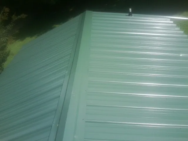 New green metal panels meeting at the ridge of a roof — Flat Roof Repair work by our crew in Kilmarnock