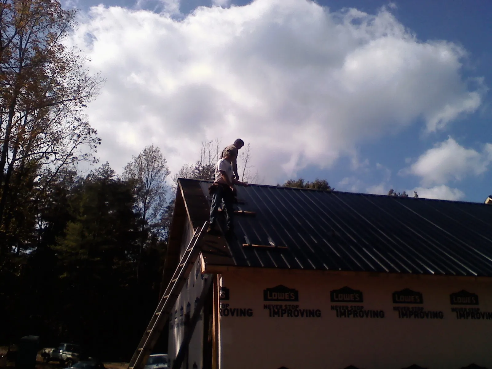 Roofer fastening dark metal panels high against a cloudy sky, from a Roof Inspection job in Kilmarnock