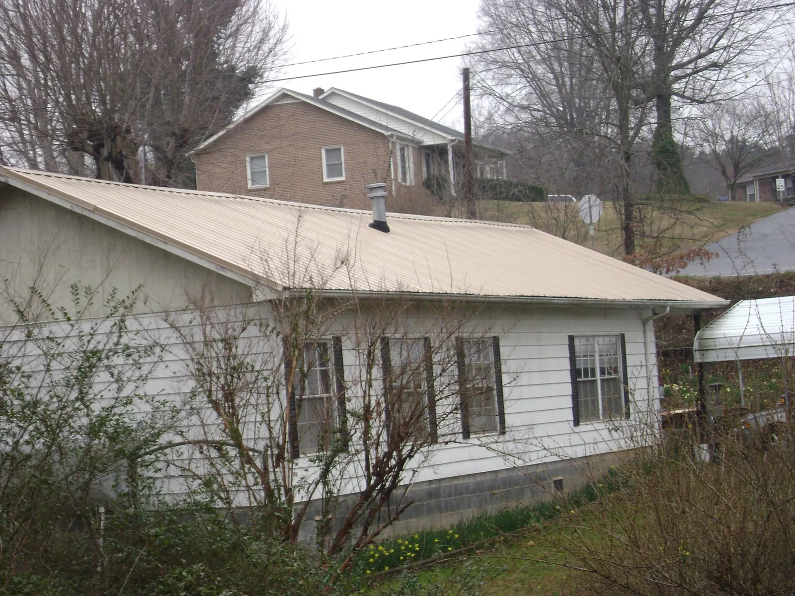Tan metal roof on a white sided house set into a hillside — Commercial Roofing by Roofing Brothers in Kilmarnock